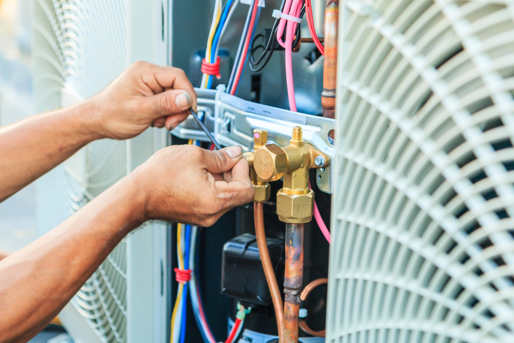 A technician uses tools to adjust wiring and components inside an HVAC unit.